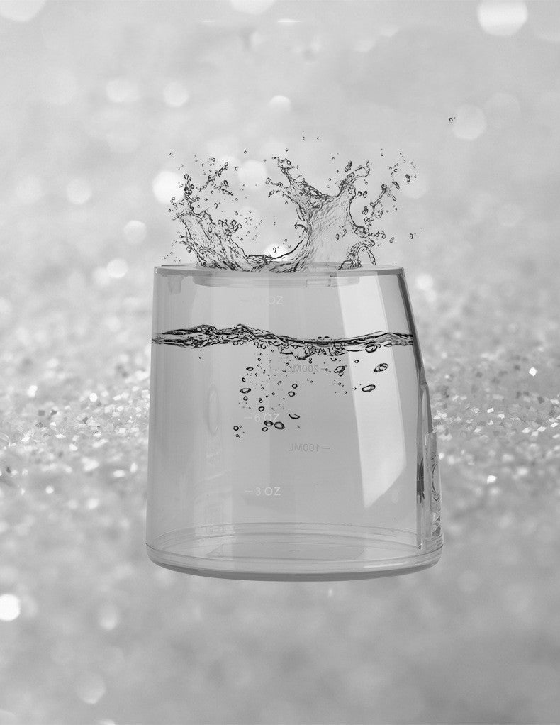 Clear glass with water splashing into it against a blurred gray background