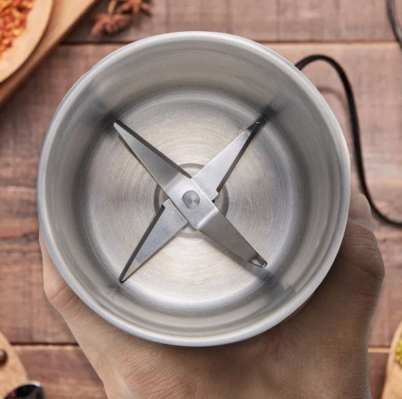 Hand holding a silver blender container with a blade on a wooden surface