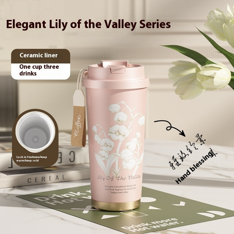 Pink ceramic tumbler with floral design on a table with books and flowers.
