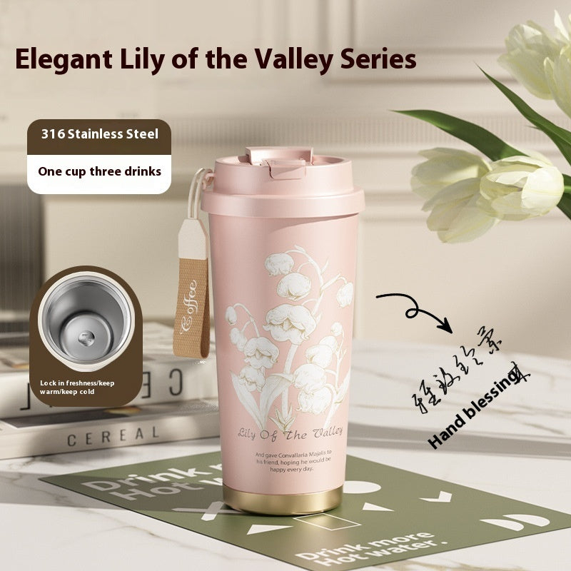Pink insulated tumbler with floral design on a table with books and flowers.