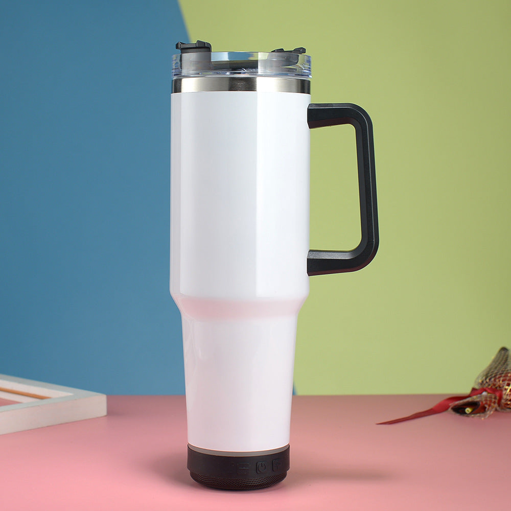 White travel mug with black handle on a pink surface against a blue and green background