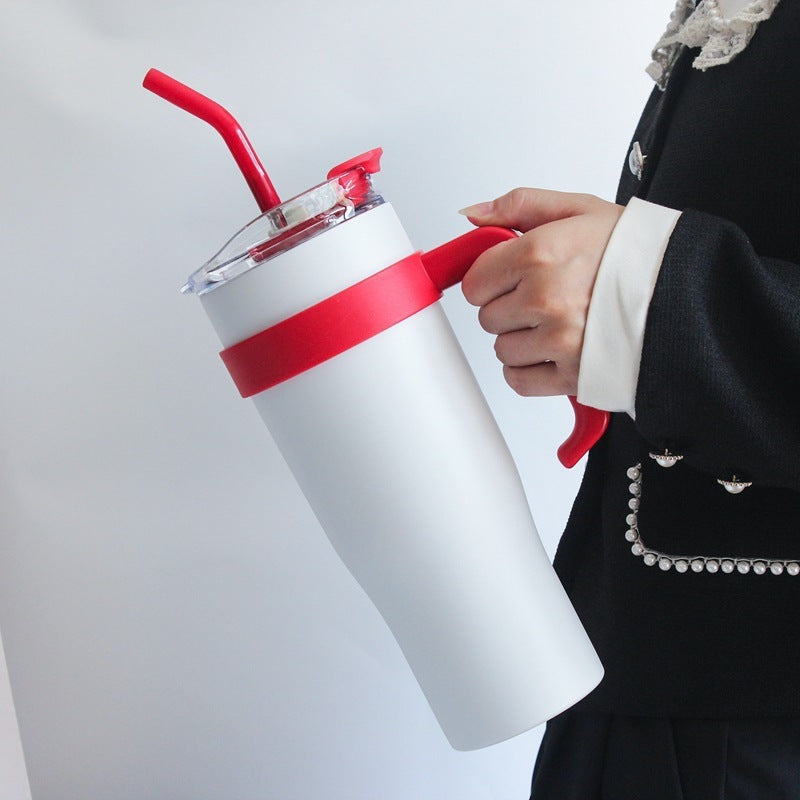 White tumbler with red lid and straw held by a person in formal attire.