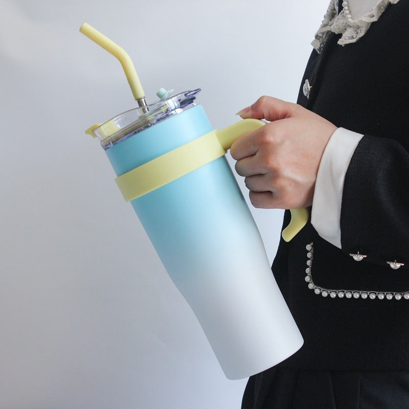 Person holding a gradient blue to white tumbler with a yellow straw and handle against a light gray background