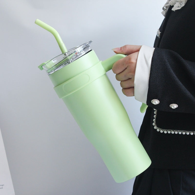Person holding a light green insulated tumbler with a straw against a plain background