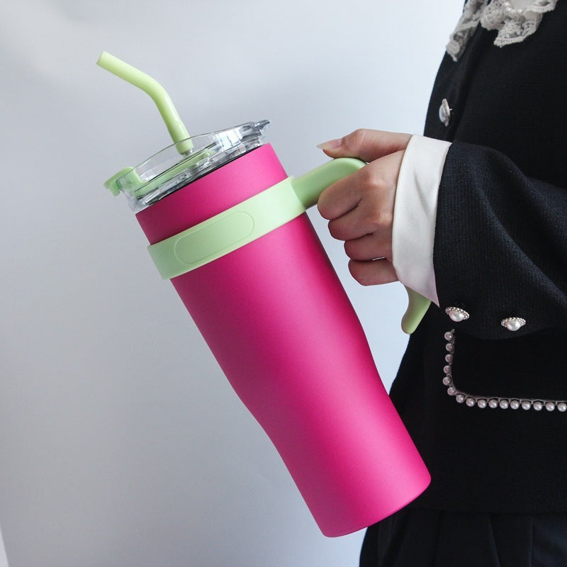 Person holding a red insulated drink container with a green straw and handle against a light gray background